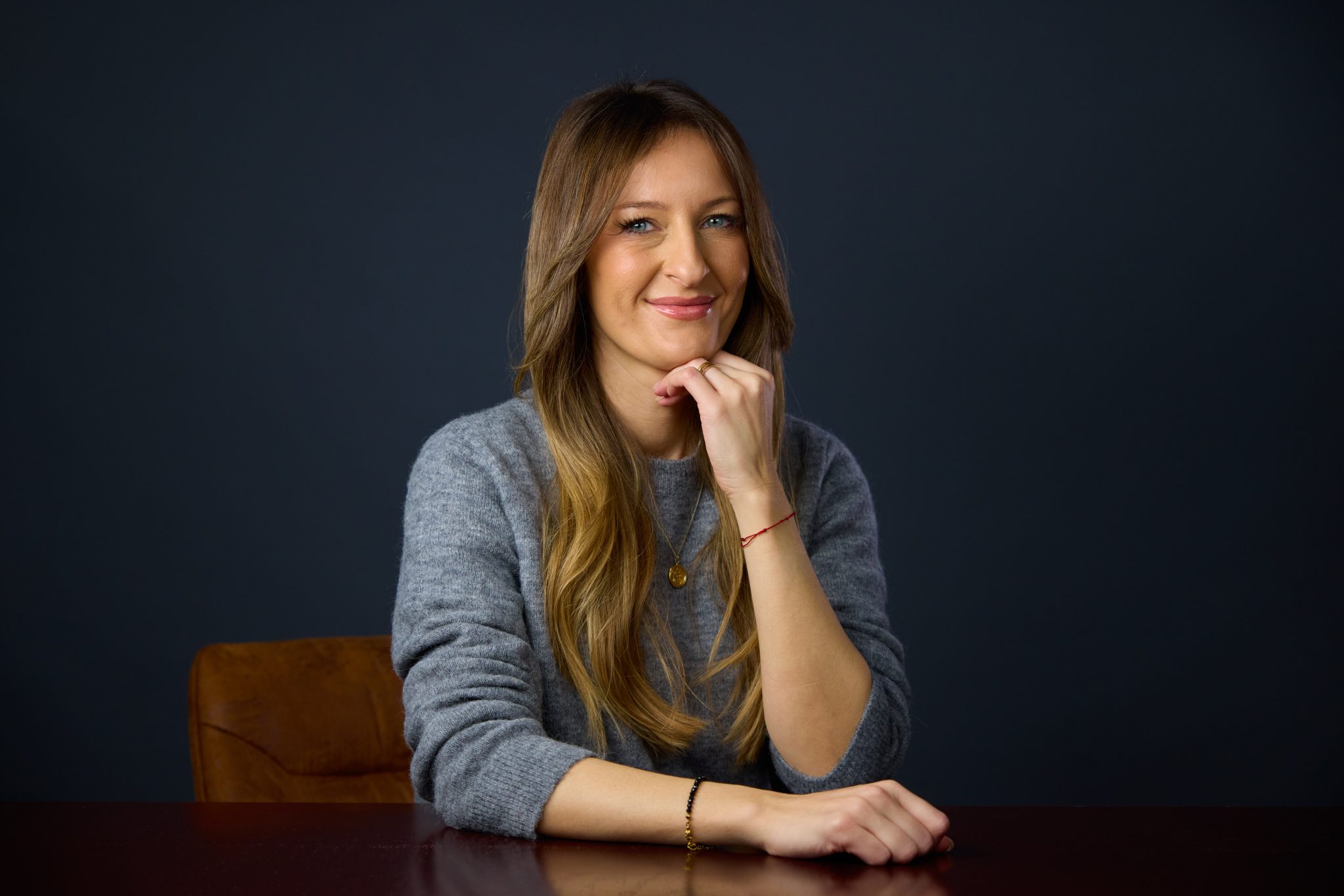 Clara Munteanu trägt einen grauen Pullover uns sitzt, lächelnd der Kamera zugewandt an einem Tisch (Bild von Neri Kranz)