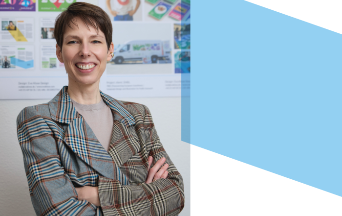 Eva Klose steht lächelnd mit dem Rücken zu einer Wand, an der viele ihrer Designs hängen. (Bild von Neri Kranz)