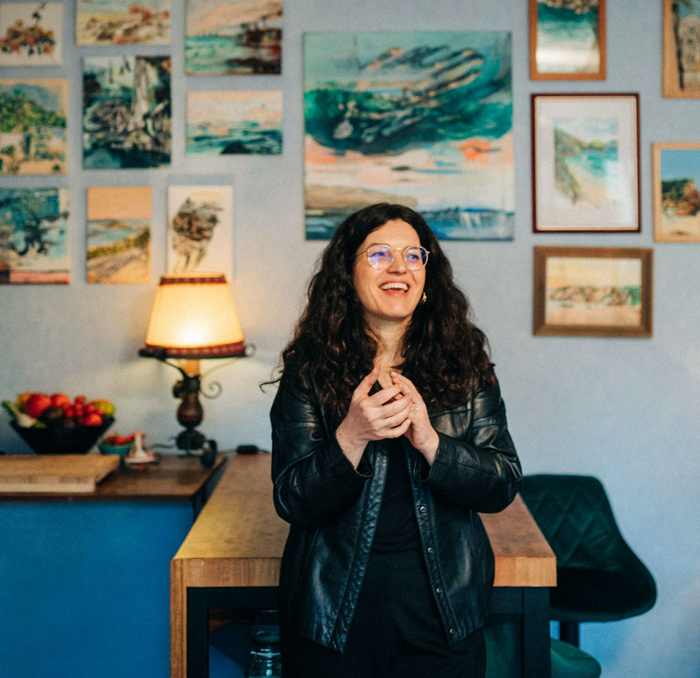 Die Künstlerin Sabine Geierhos, die vor einer mit ihren Kunstwerken bestückten Wand steht