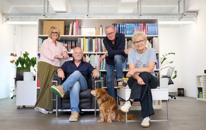 Das Team von wsp design - 2 Frauen und 2 Männer - sitzt bzw. steht vor einem Bücherregal. In der Mitte sitzt ein Hund (Bild von Neri Kranz).